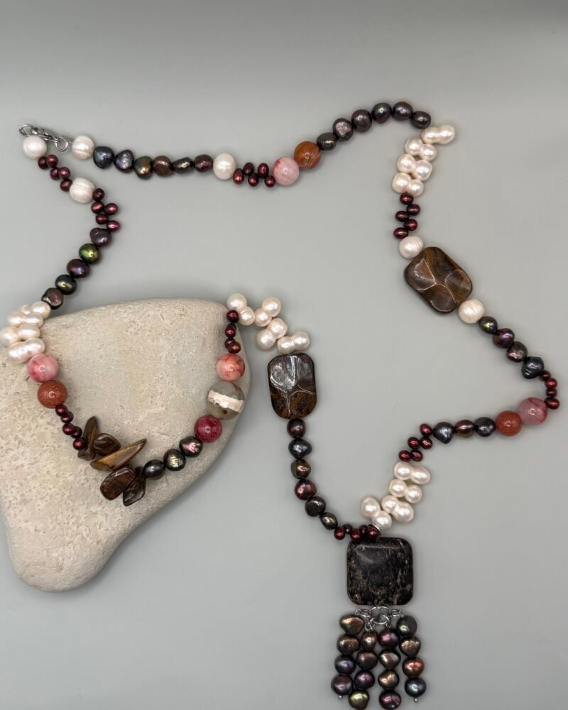 Collar con perlas cultivadas blancas y oscuras, piedras naturales en tonos tierra y rojizos, y un dije central de piedra oscura