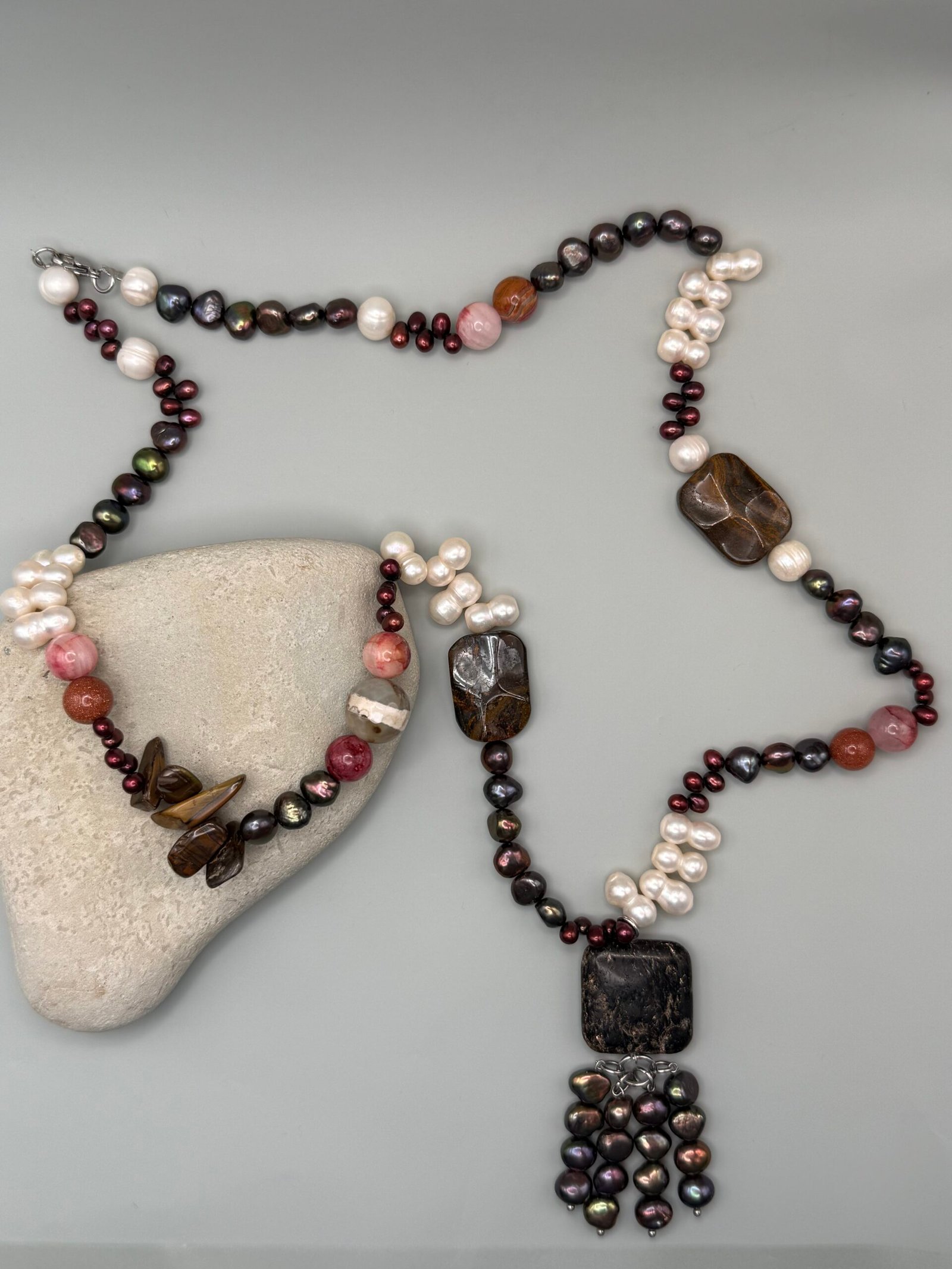 Collar con perlas cultivadas blancas y oscuras, piedras naturales en tonos tierra y rojizos, y un dije central de piedra oscura